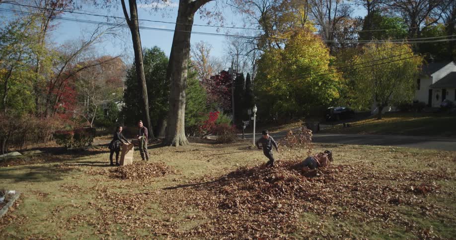 A clip of children playing with leaves while mother and father are cleaning