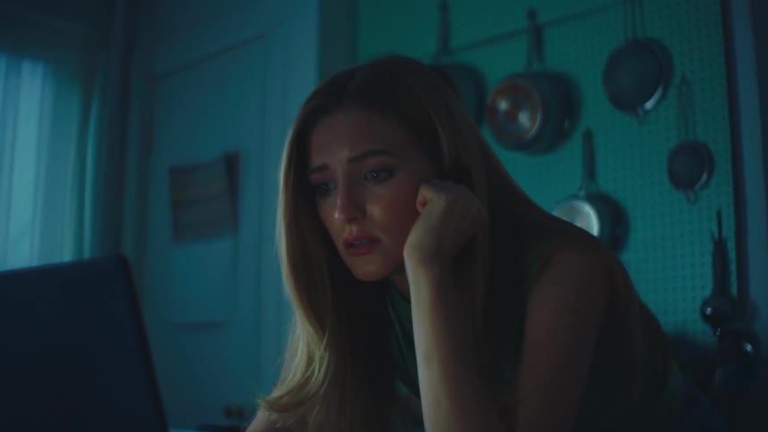 Blonde woman with shocked expression and crying looking at a laptop in the kitchen