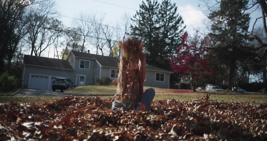Little girl sitting on a grassy yard with dry autumn leaves