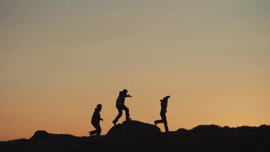 Silhouette of friends running on a trail over rocks at sunset