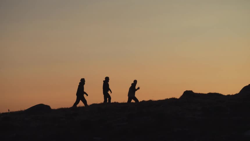 Three friends are hiking on a landscape while the sun is setting