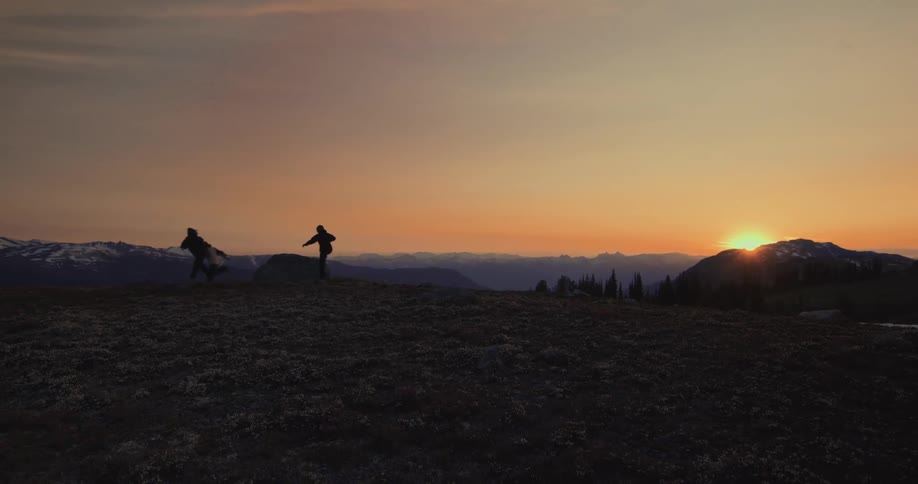 Silhouette of three people running down a mountain with the sunrise on the horizon