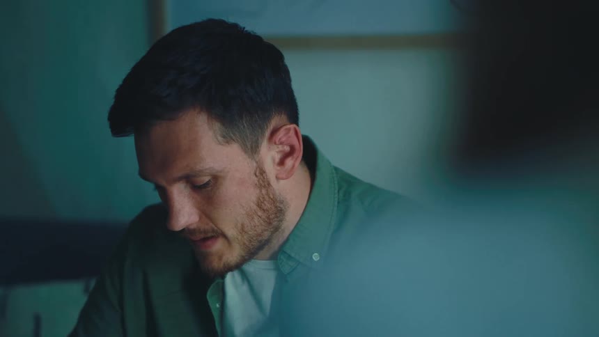 A bearded man wearing a green shirt and a white top talks on the phone and then hangs up
