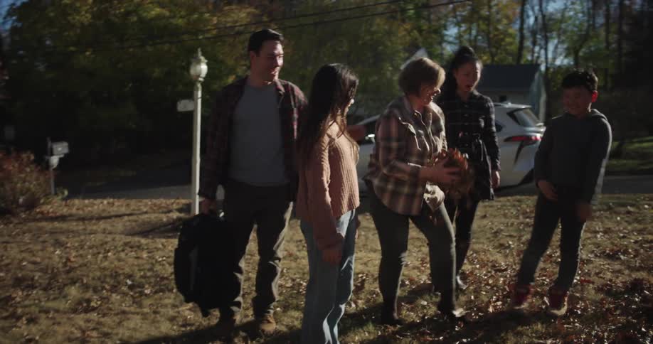 Family walking together in the backyard of a house full of dry autumn leaves