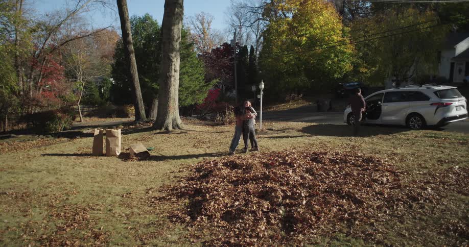 A family gathers fallen leaves into a pile in their yard on a sunny autumn day