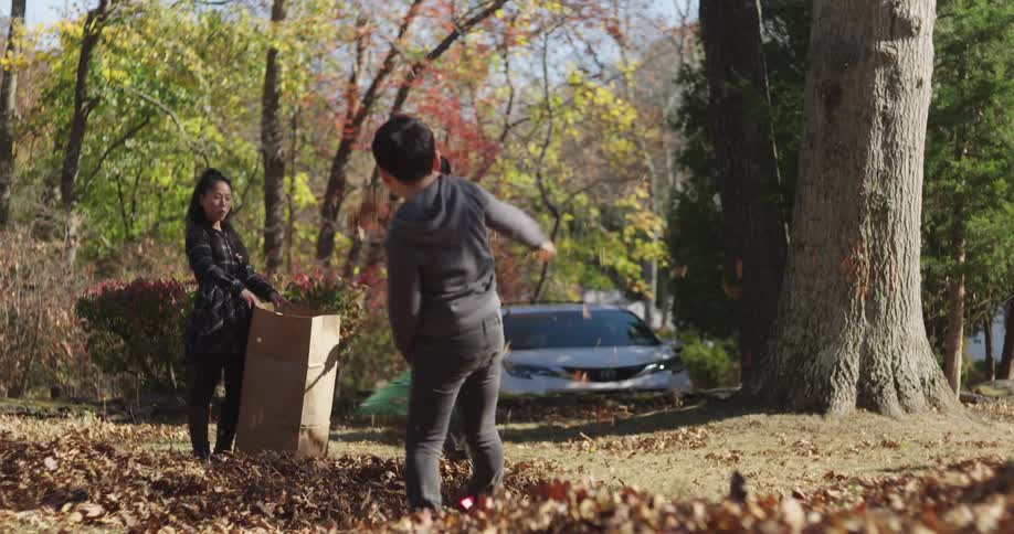 Father and mother holding a cardboard box and their little boy throwing a ball of dry leaves