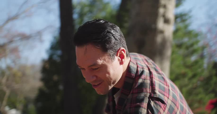A man is smiling and picking up several dry leaves with a rake and putting them in a bag that is being held by a woman