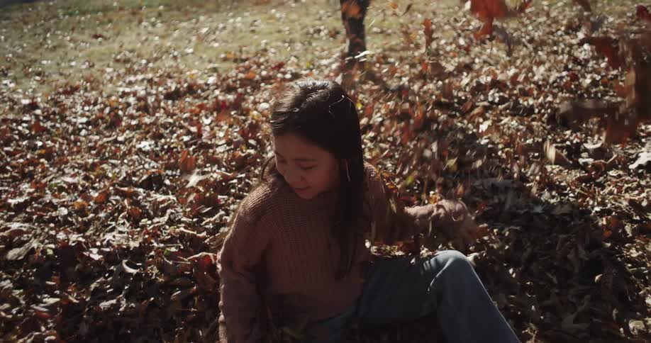 A young girl smiles and laughs tossing leaves into the air