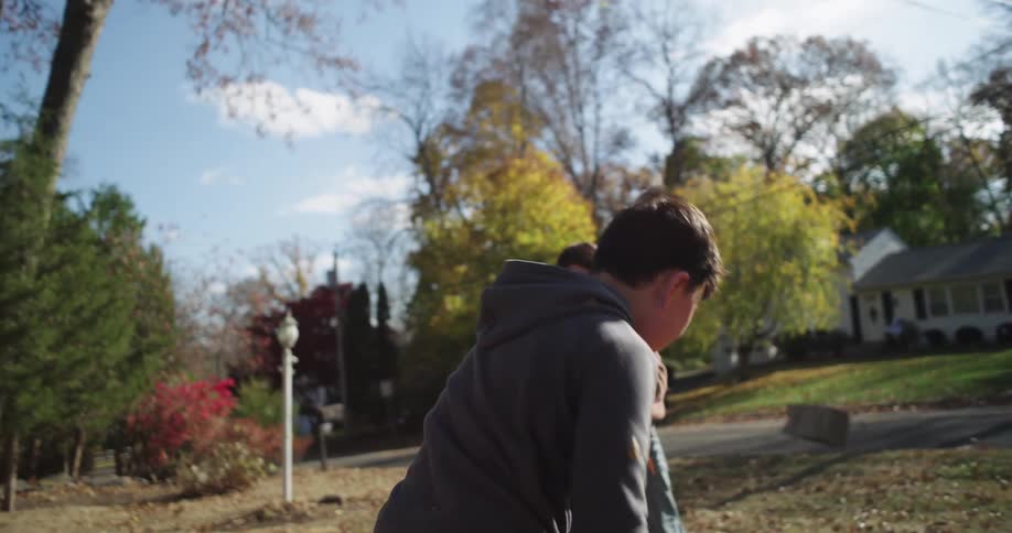 A brother and sister play with autumn leaves on a partly sunny day