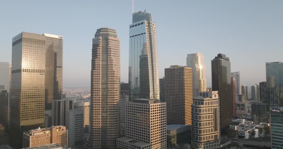The sunlit los angeles skyline dominated by towering skyscrapers stretches into the hazy distance