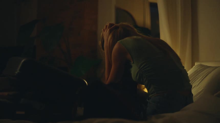 Blonde woman with hands on head sitting dejectedly on the bed in the bedroom