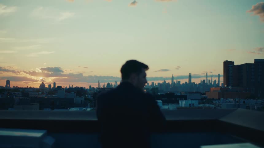 Man standing on a balcony admiring the city skyline at sunset