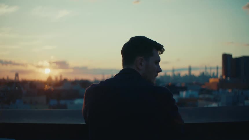 A man stands overlooking a city at sunset with vibrant colors illuminating the skyline