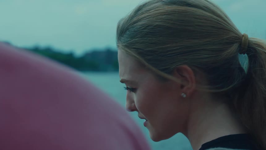 Close up of a woman with blonde hair talking to someone else near a lake or river