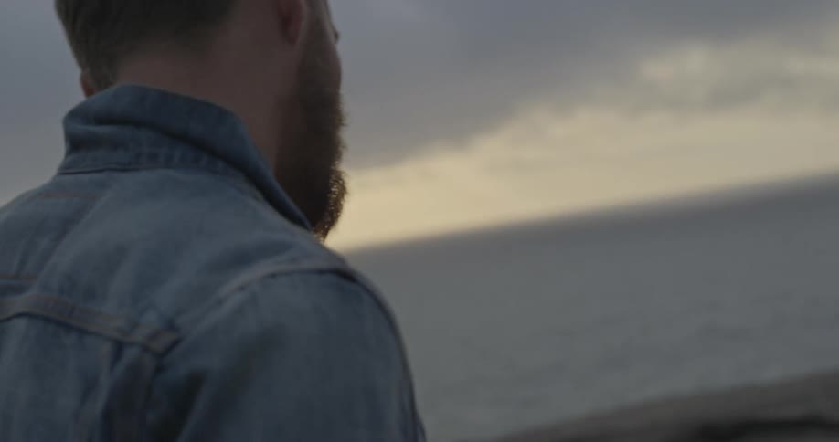 A man in a denim jacket walks towards the ocean