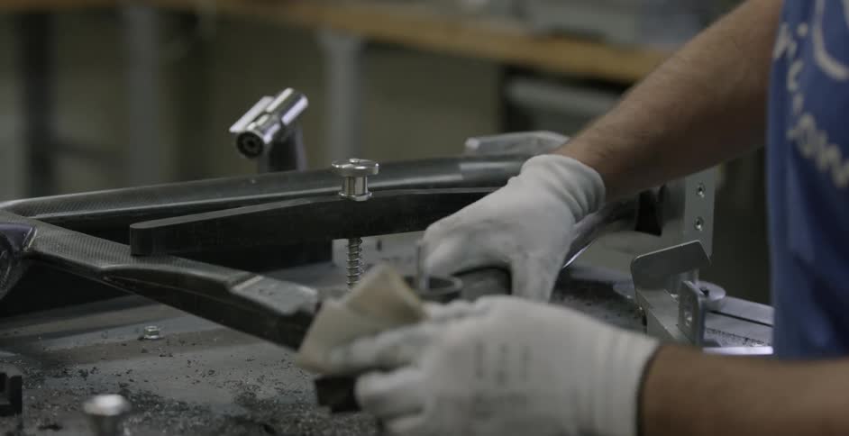 Person wearing white gloves tightens a screw in a metal object and buffs it