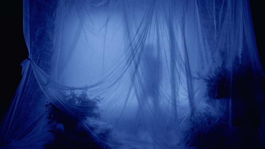 The silhouette of a person behind a large white sheet spread out in the dark room