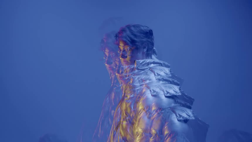 Model in multiple exposures wearing a silver jacket and glasses