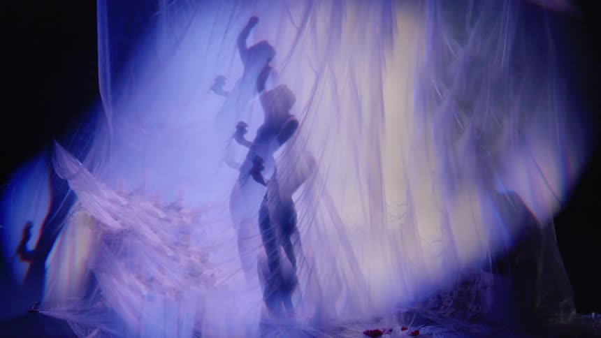 The silhouette of a person standing behind a huge white sheet doing some slow dance moves
