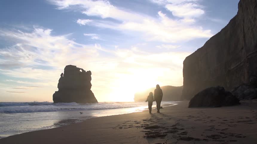 Woman and child walking on a sandy beach at sunset
