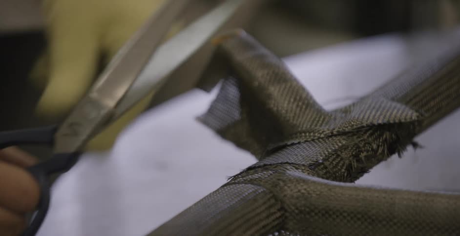 A worker is using scissors to trim pieces of mesh fabric