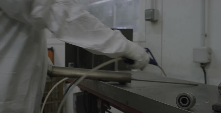 Person in a lab coat spays down a piece of metal