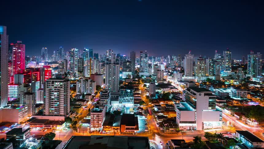 A vibrant cityscape at night features illuminated skyscrapers glowing streets and dynamic car trail lights as vehicles speed by below