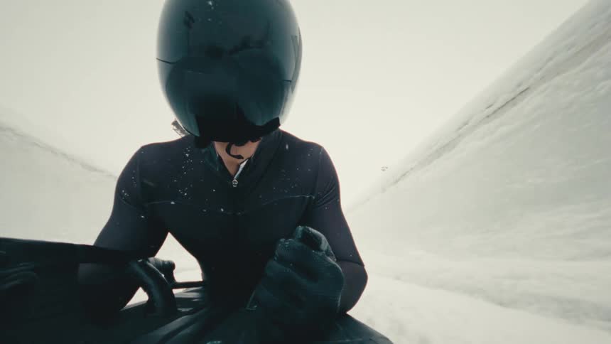Person rides a skeleton sled down an icy channel during winter