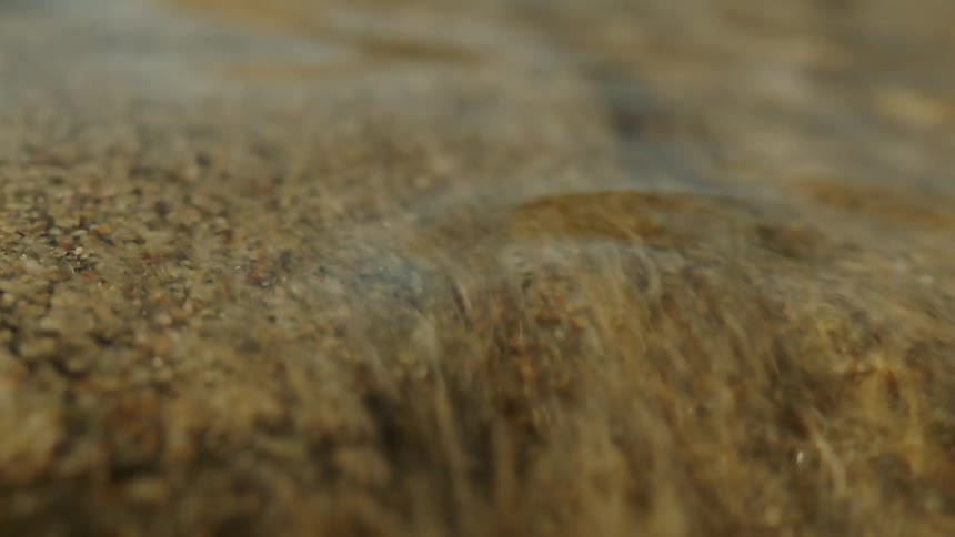 A small stream of clear water passing over a sandy soil