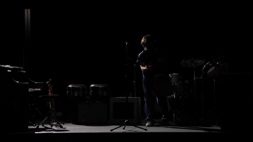 Male walks onto stage filled with instruments and picks up a guitar