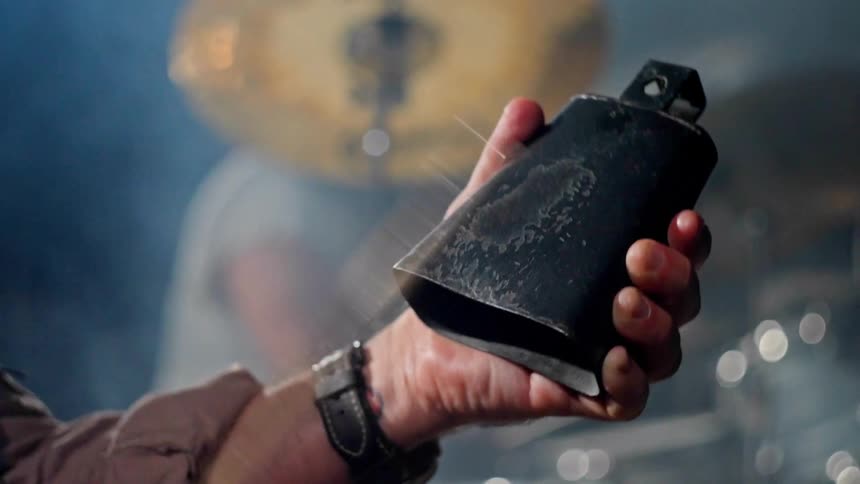 A persons hand holding a small metal bell and with the other hand using a twig to strike the bell