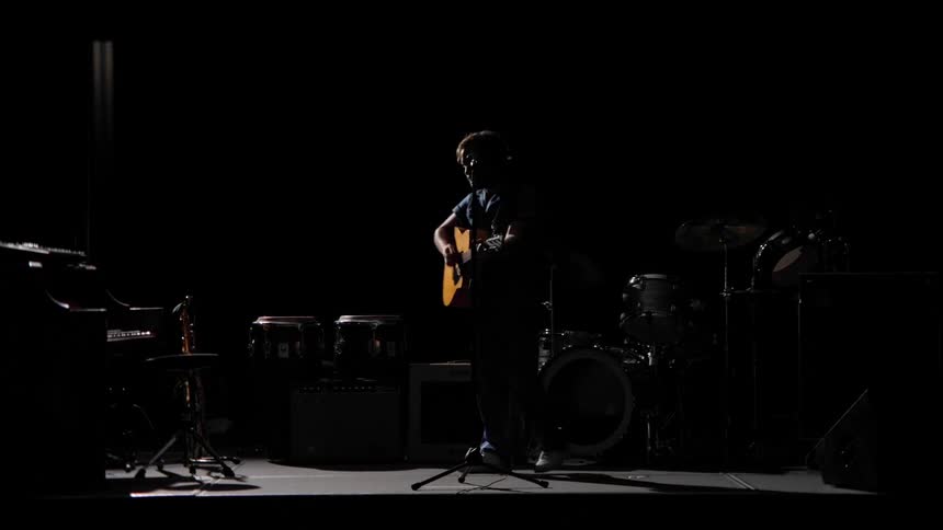 Man is performing by himself on a dark lit stage
