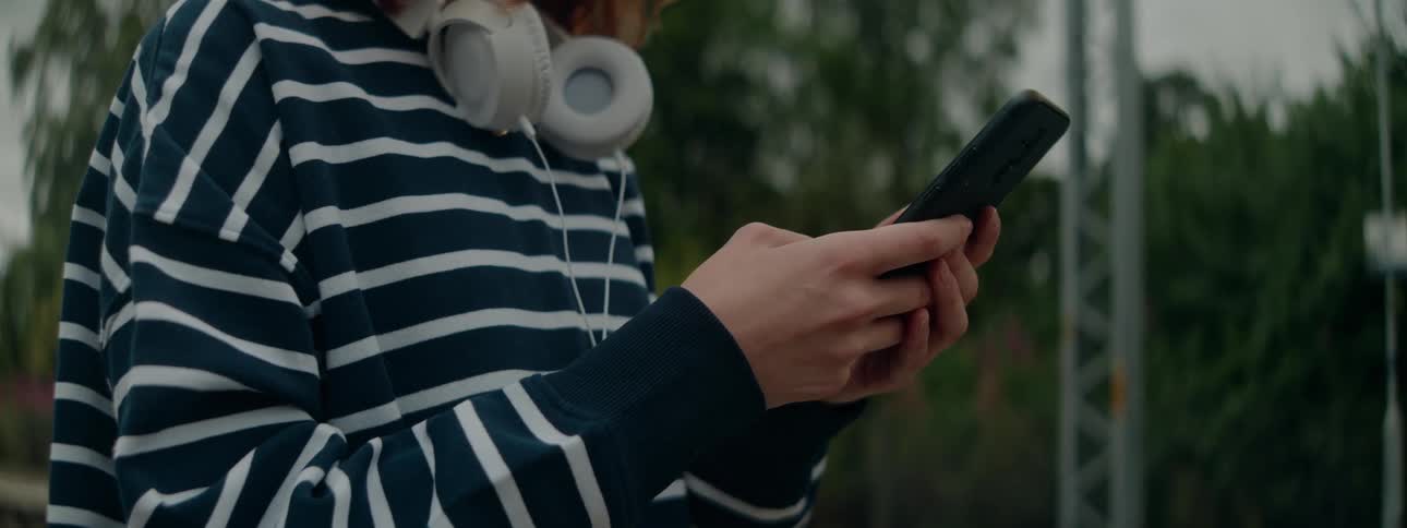 Redhead stands outdoors and texts on her smartphone