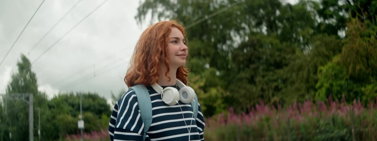 Redhead woman with white headphones around her neck in an outdoor area
