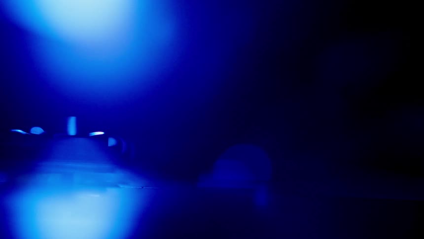 The video shows a dark scene lit only by a bright blue light source with an indistinct object partially visible in the foreground