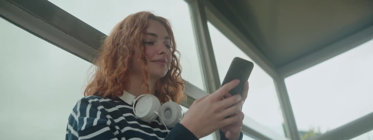 Young redhaired woman with curly hair sitting interacting with a smartphone