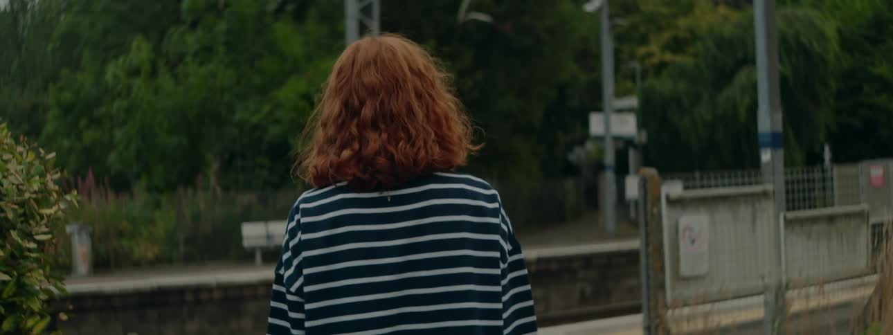 A redhaired woman with her back turned wearing a black and white striped shirt is walking in an area with a terminal in front of her