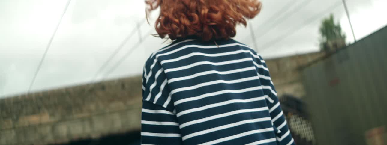 A redhaired woman in a black and white shirt is standing and behind her there are moving train cars