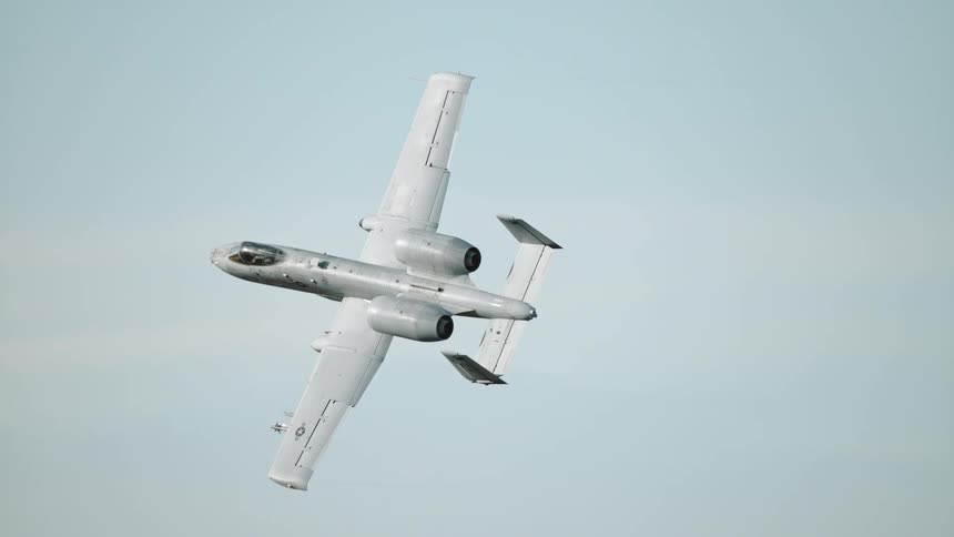 An a10 warthog attack aircraft banks in a gentle turn against a pale blue sky