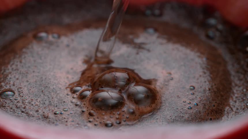 Water being placed in a container that is filled with a black and viscous liquid with some bubbles where the water has fallen