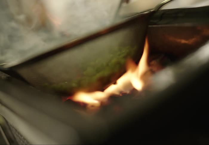 A stainless steel wok with steaming green vegetables sits on a glowing hot stovetop