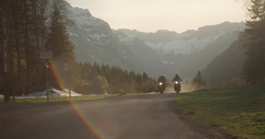 People on two motorcycles on a road surrounded by snowy mountains