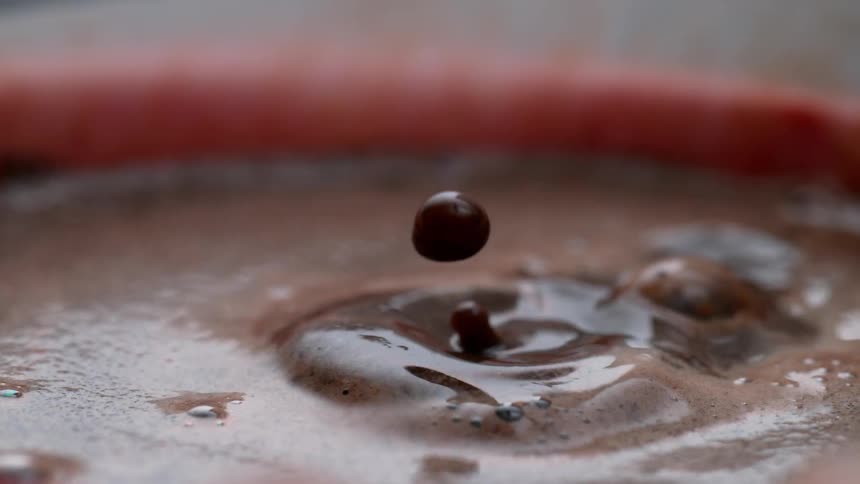 A transparent drop falling on a surface of dense black liquid and making ripples