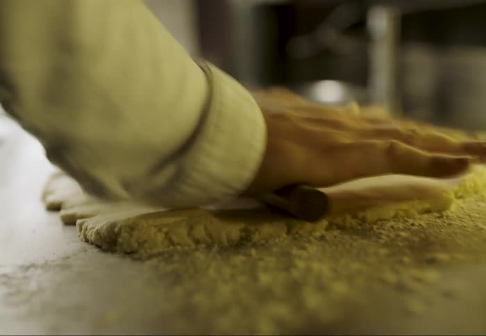 Human hands using a cylindrical wooden object to knead dough