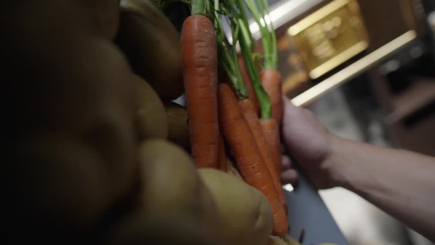 Hand carrying a box with vegetables including carrots