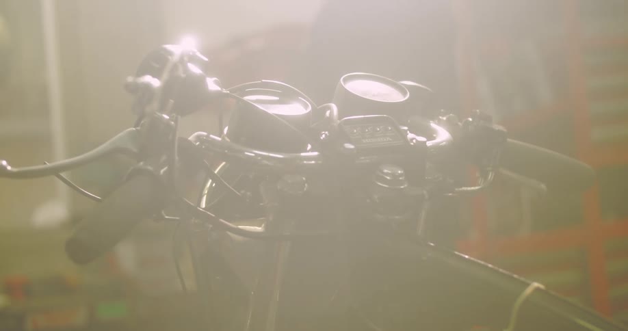 Closeup of a motorcycles handlebars in an indoor environment with sunlight reflecting off it