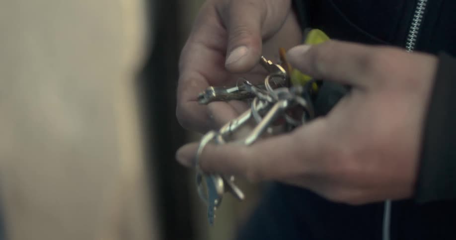 Man takes a key chain from his pocket and looks for a key while standing near an exterior door