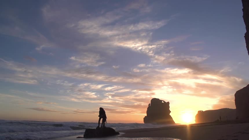 A person stands on a rock on the beach at dawn