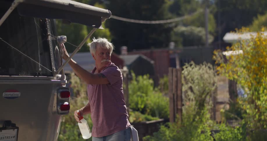 Elderly man cleaning the rear side of a vehicle and his wife comes alongside him