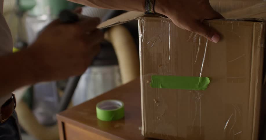 Hand sticking a green tape on a cardboard box and with a pen writing on top
